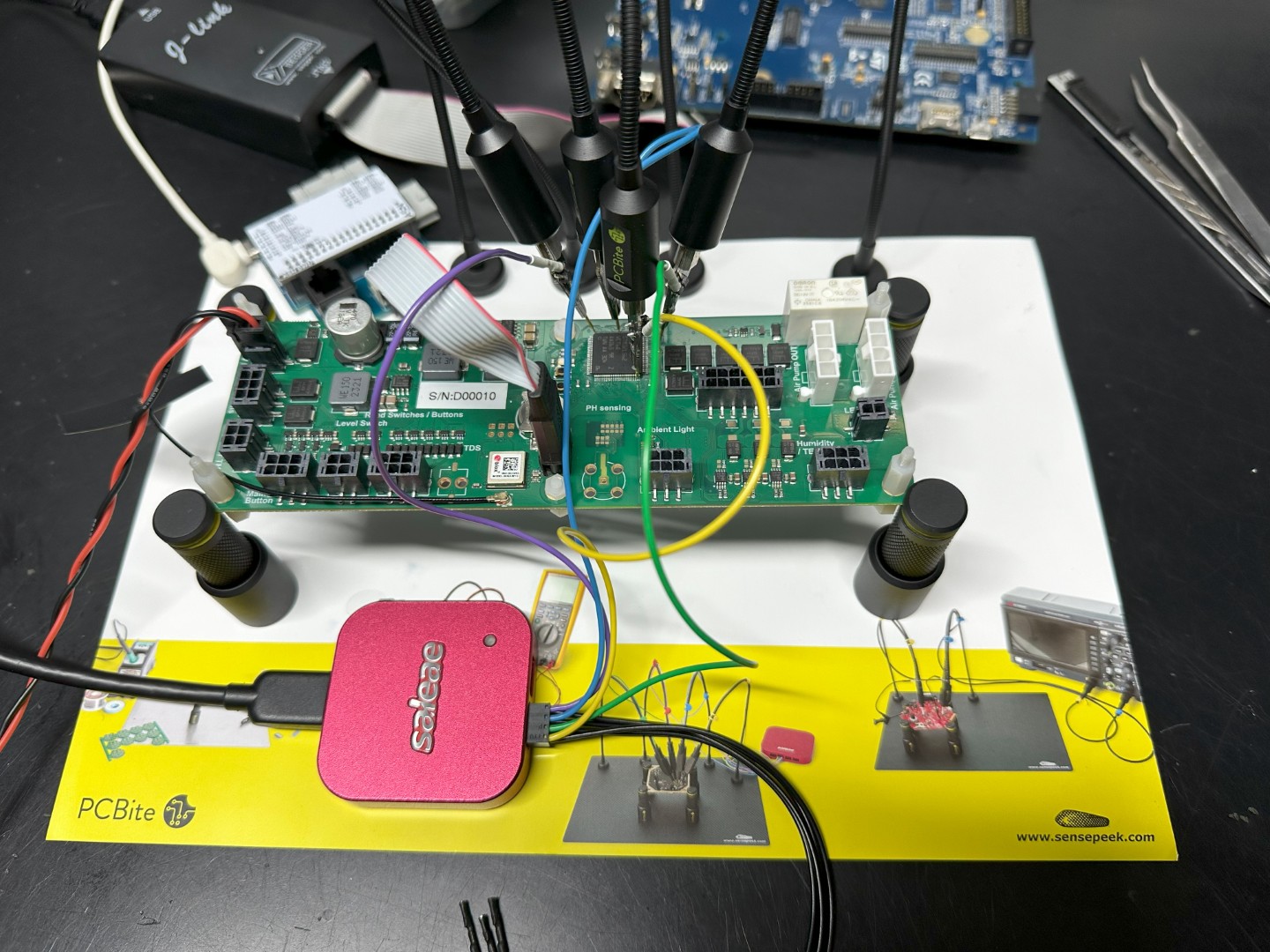 Custom PCB on the bench under probes with a logic analyser and J-Link attached